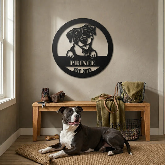 Dog lying on a rug in front of a wall with a metal plaque featuring a dog's face and 'PRINCE EST 2021' text.